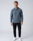 Full-body studio view of an athletic male model wearing the MOVE Sport Apparel men’s waffle hoodie in Blue Heather Ashes with black training pants and white athletic shoes.