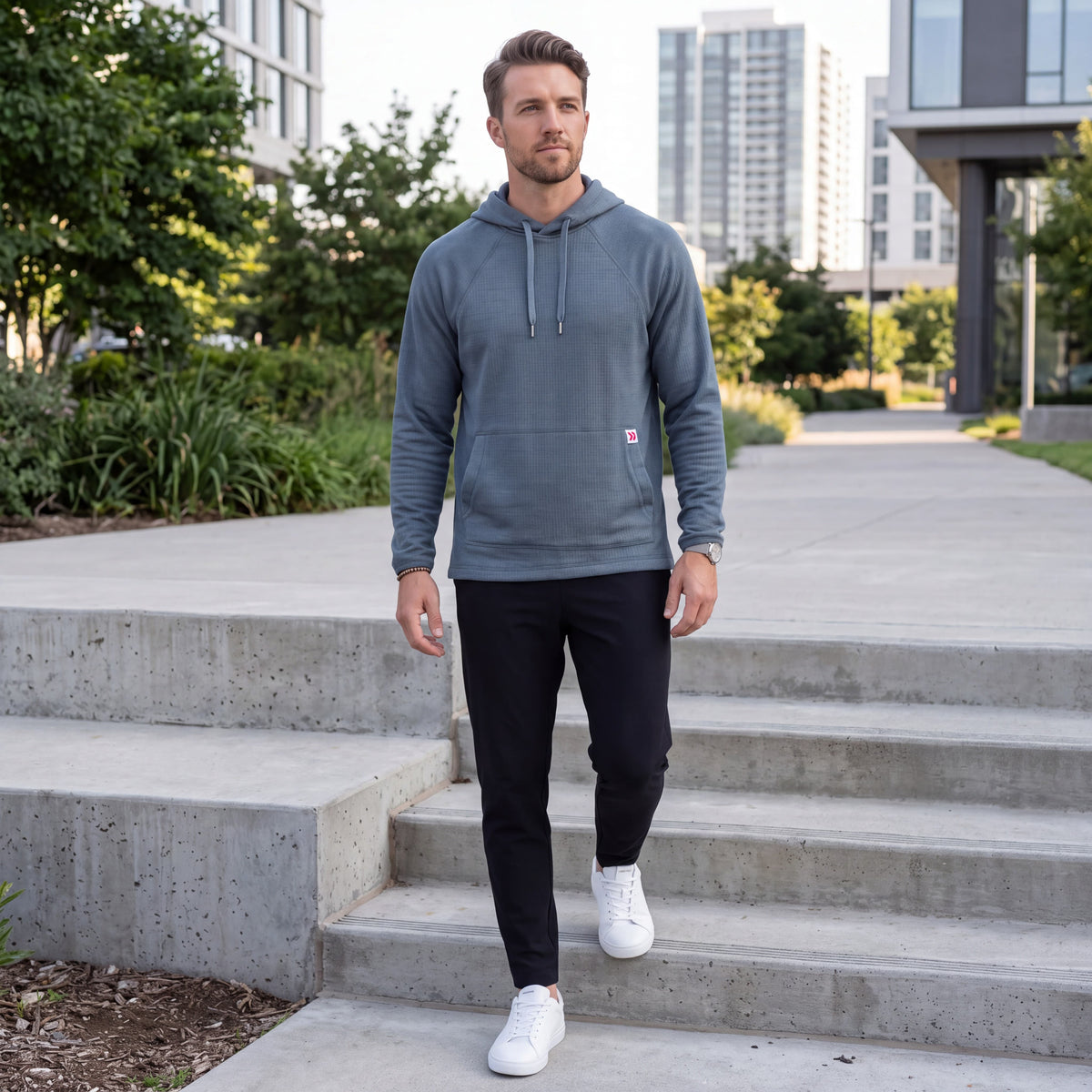 Athletic male model walking down concrete steps in the MOVE Sport Apparel men’s waffle hoodie in Blue Heather Ashes, black training pants and white athletic shoes.