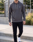 Male model wearing the charcoal MOVE Sport Apparel waffle pullover hoodie while walking on outdoor concrete steps.