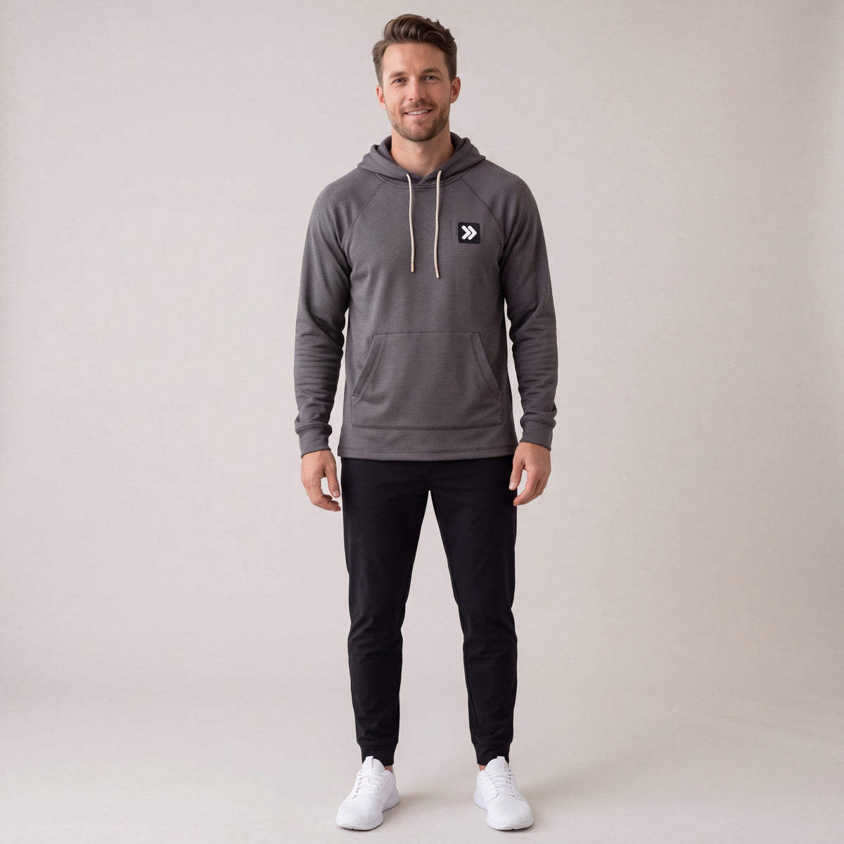 Full-body male model wearing the charcoal MOVE Sport Apparel waffle pullover hoodie with black pants in a neutral studio.