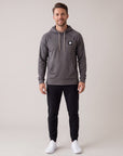 Full-body male model wearing the charcoal MOVE Sport Apparel waffle pullover hoodie with black pants in a neutral studio.
