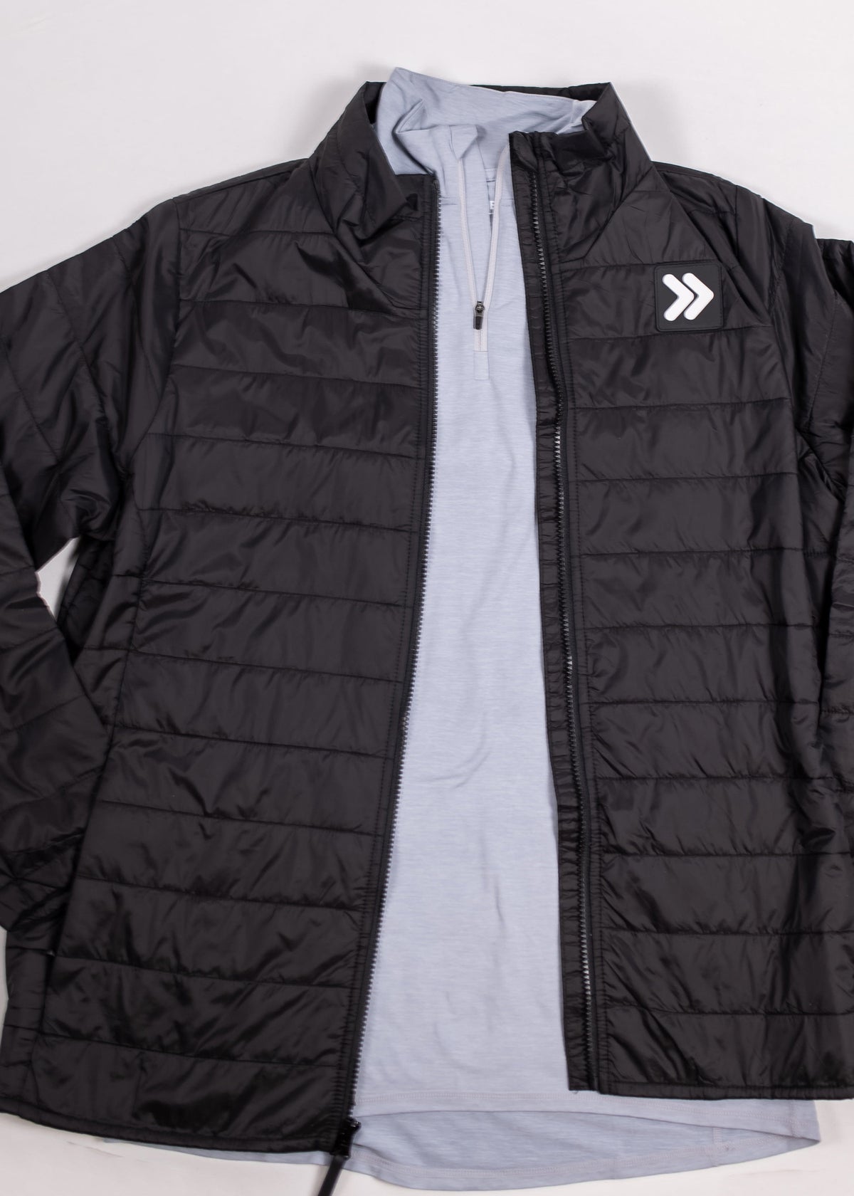 Open black quilted jacket showing the original chest patch and layered quarter zip.