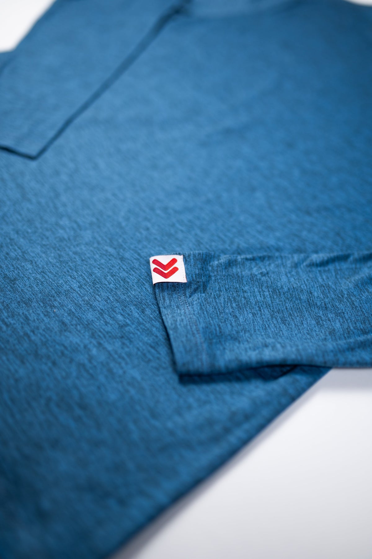 Close view of the red-and-white cuff label and fabric texture on the Blue Mirage MOVE Sport Apparel Men’s Essential Long Sleeve.
