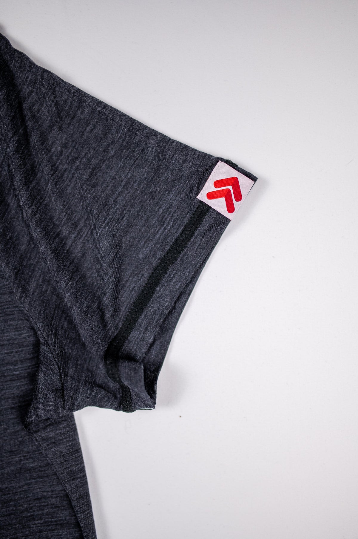 Close-up of the original white tab with red double chevrons at the Asphalt merino tee sleeve hem.