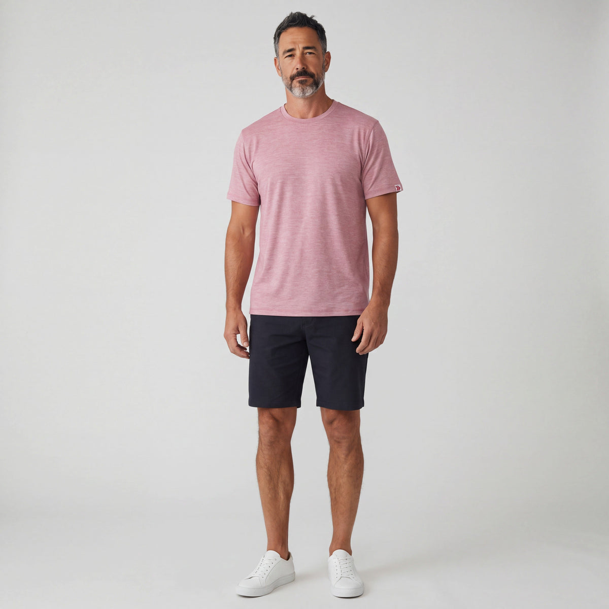Full-body studio view of a man wearing MOVE Sport Apparel men’s Essential Short Sleeve in Heather Crimson with dark shorts and white trainers.