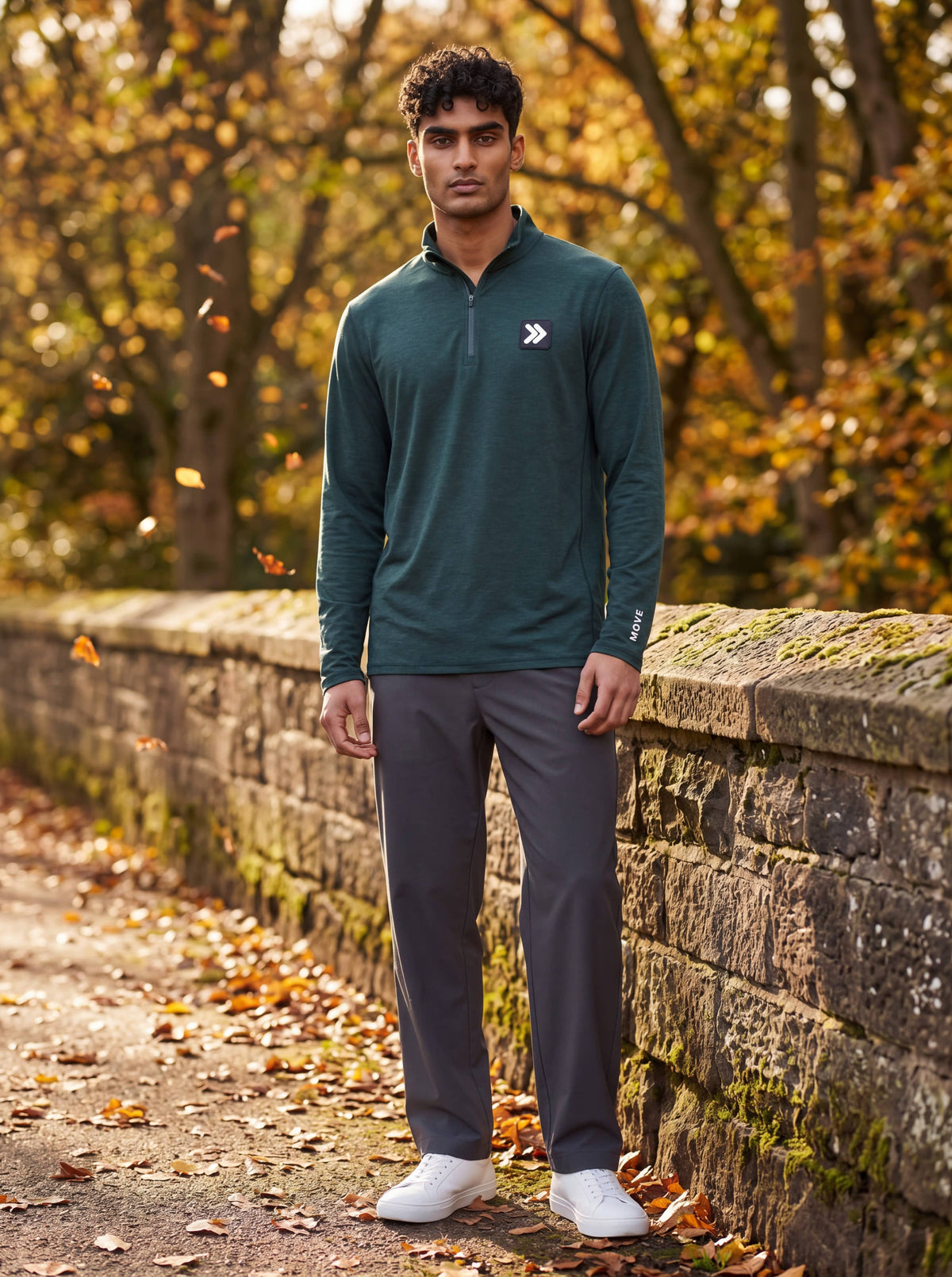 Man wearing MOVE Sport Apparel men’s Essential Quarter Zip in Pine Grove beside a stone wall on an autumn park path.