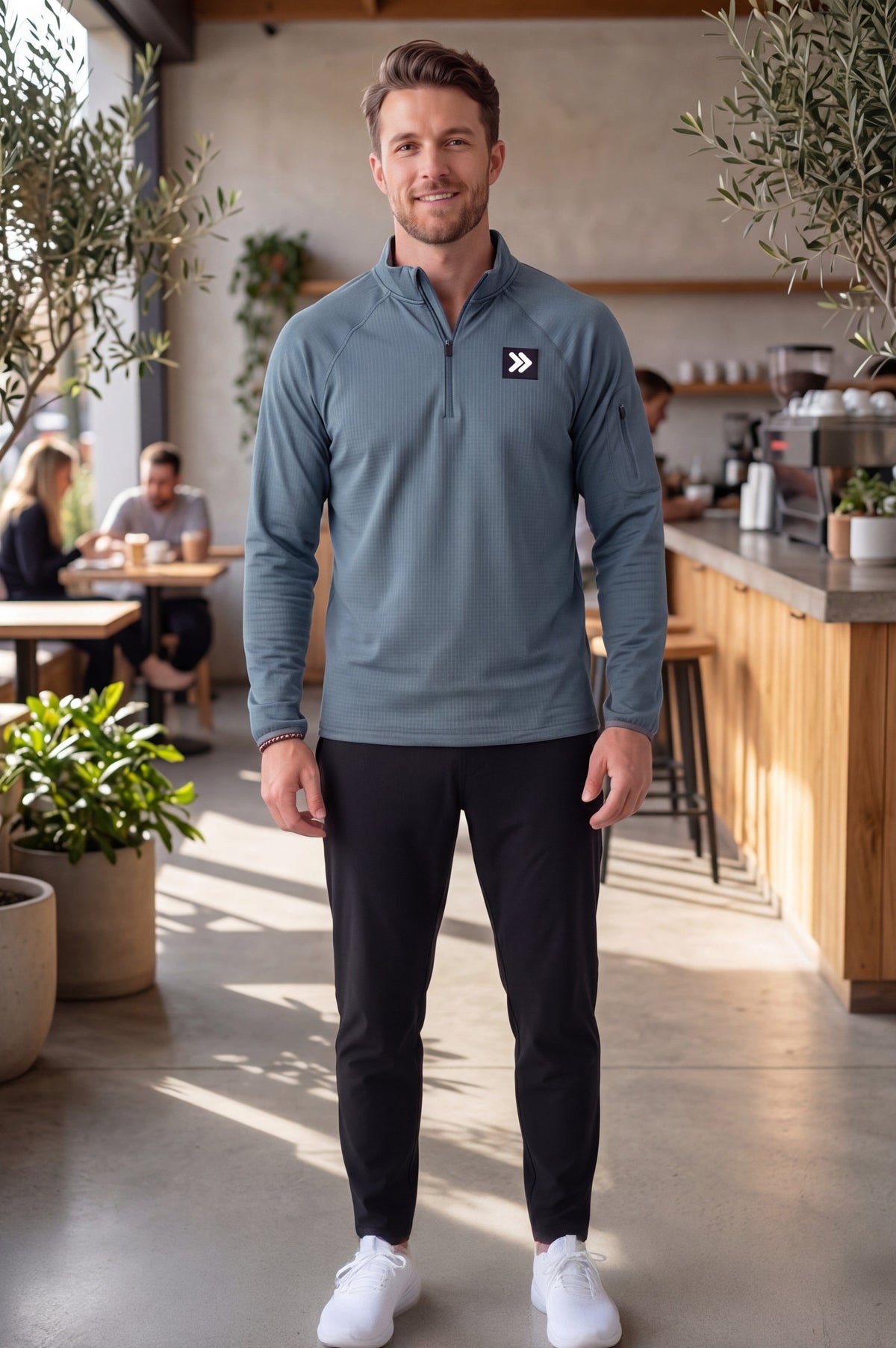 Male model wearing MOVE Sport Apparel men’s Balsam Green waffle quarter zip at a modern café with black training pants and white sneakers.