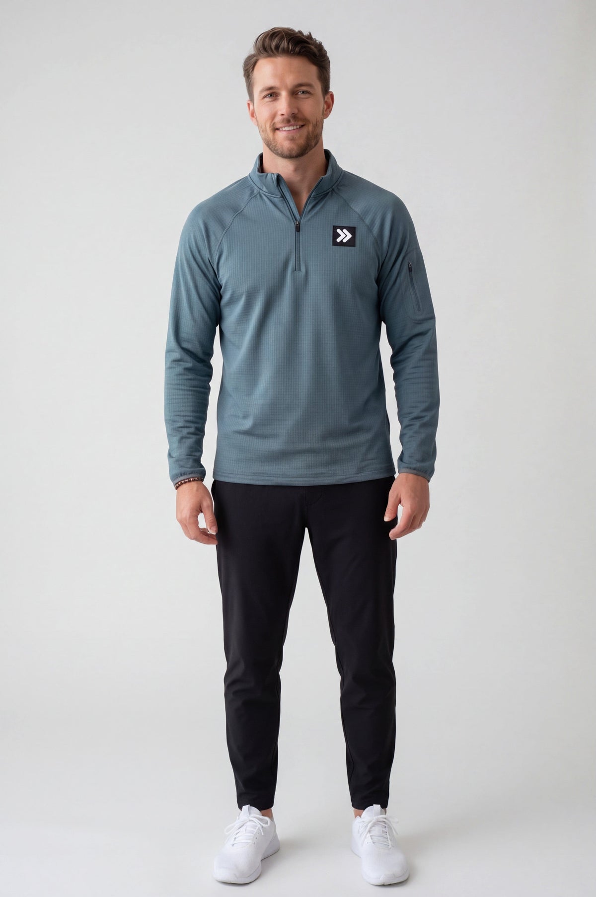 Full-body male studio model wearing MOVE Sport Apparel men’s Balsam Green waffle quarter zip with black training pants and white sneakers.
