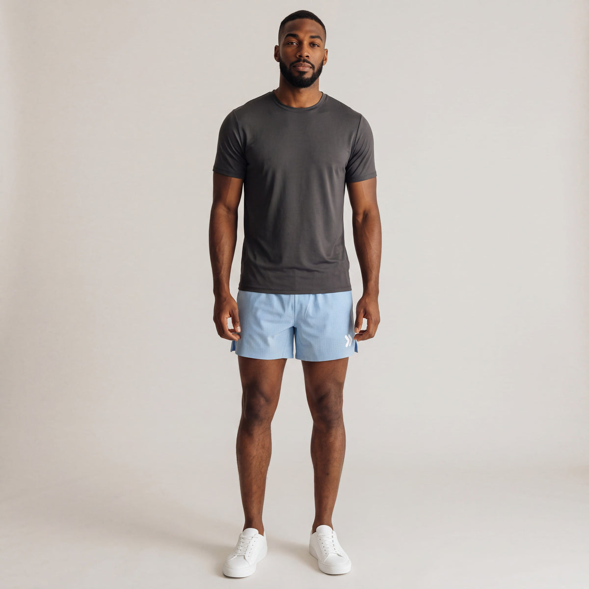 MOVE Sport Apparel Men’s Lightweight Athletic Running Shorts in Mountain Bluebird pale blue, worn by an adult man with a charcoal athletic tee and white trainers in a neutral studio, showing the original white leg embellishment.