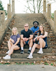 Group wearing MOVE Sport Apparel athletic outfits while seated on park steps, including a blue LuxDry tee.