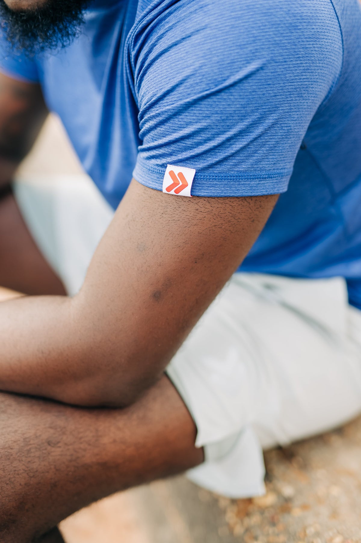 Close-up of the original red-chevron sleeve tab on a blue LuxDry tee worn outdoors.