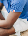 Close-up of the original red-chevron sleeve tab on a blue LuxDry tee worn outdoors.