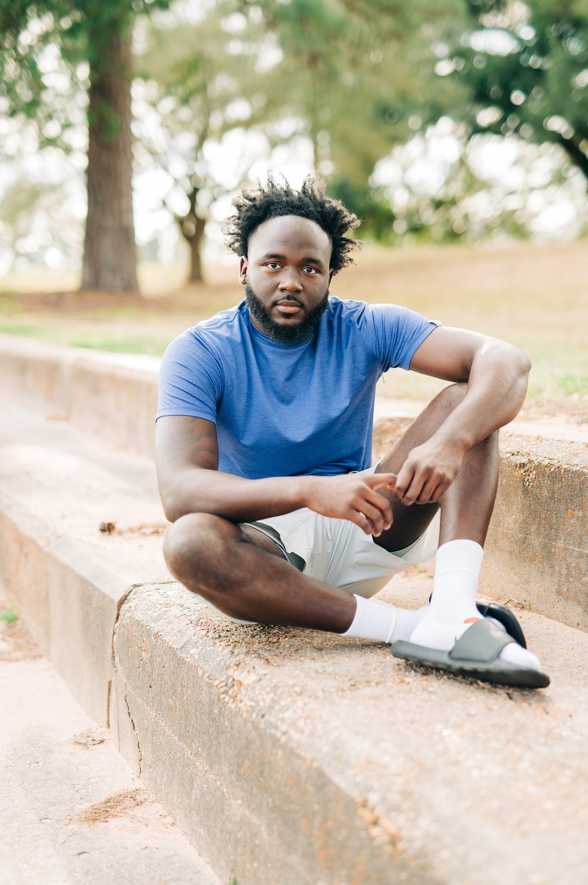 Front portrait of a man sitting outdoors wearing a blue LuxDry tee and light shorts.