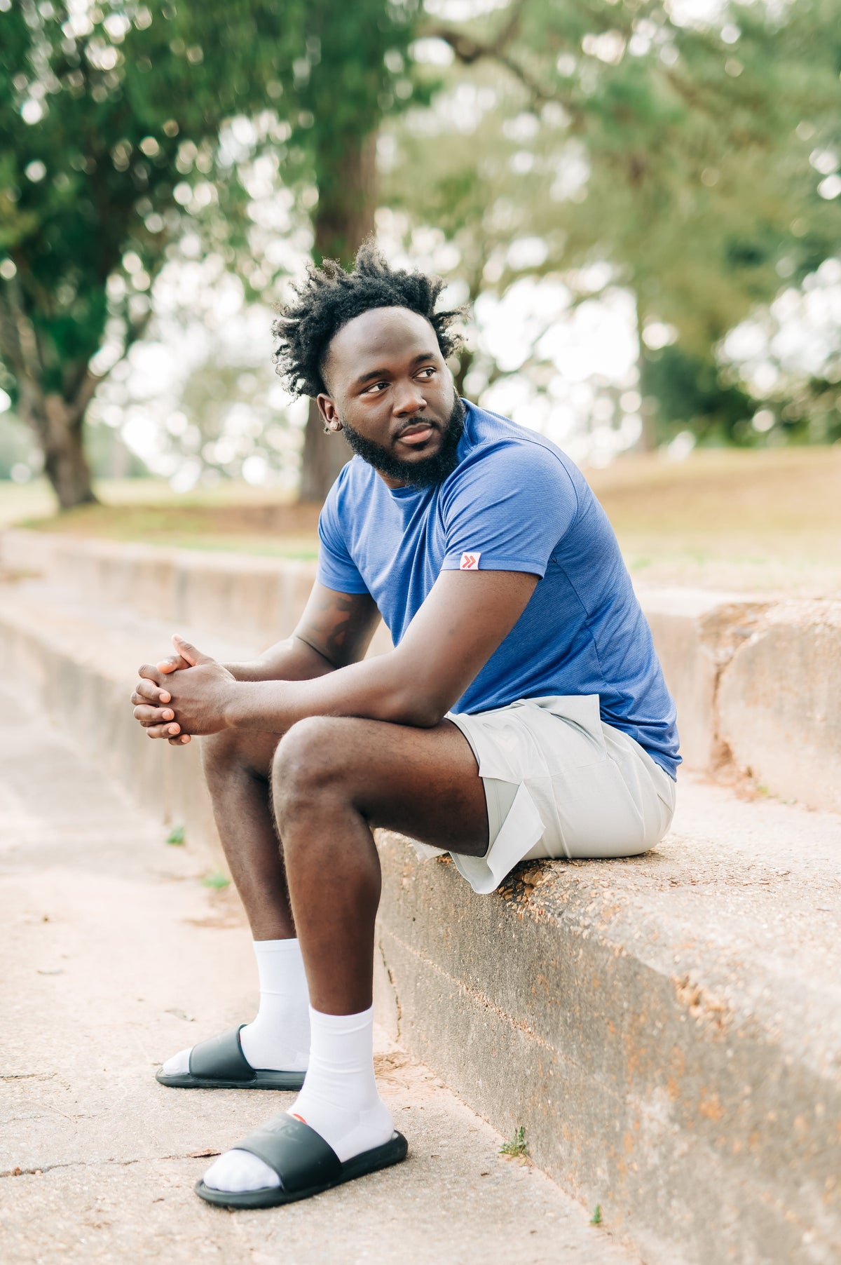 Man wearing a blue LuxDry Training T-Shirt and light shorts seated outdoors.