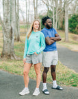 Man wearing a blue LuxDry tee beside a woman in a turquoise top on a woodland path.