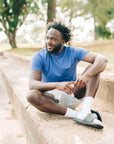 Man sitting in a relaxed pose outdoors wearing a blue LuxDry tee and light shorts.
