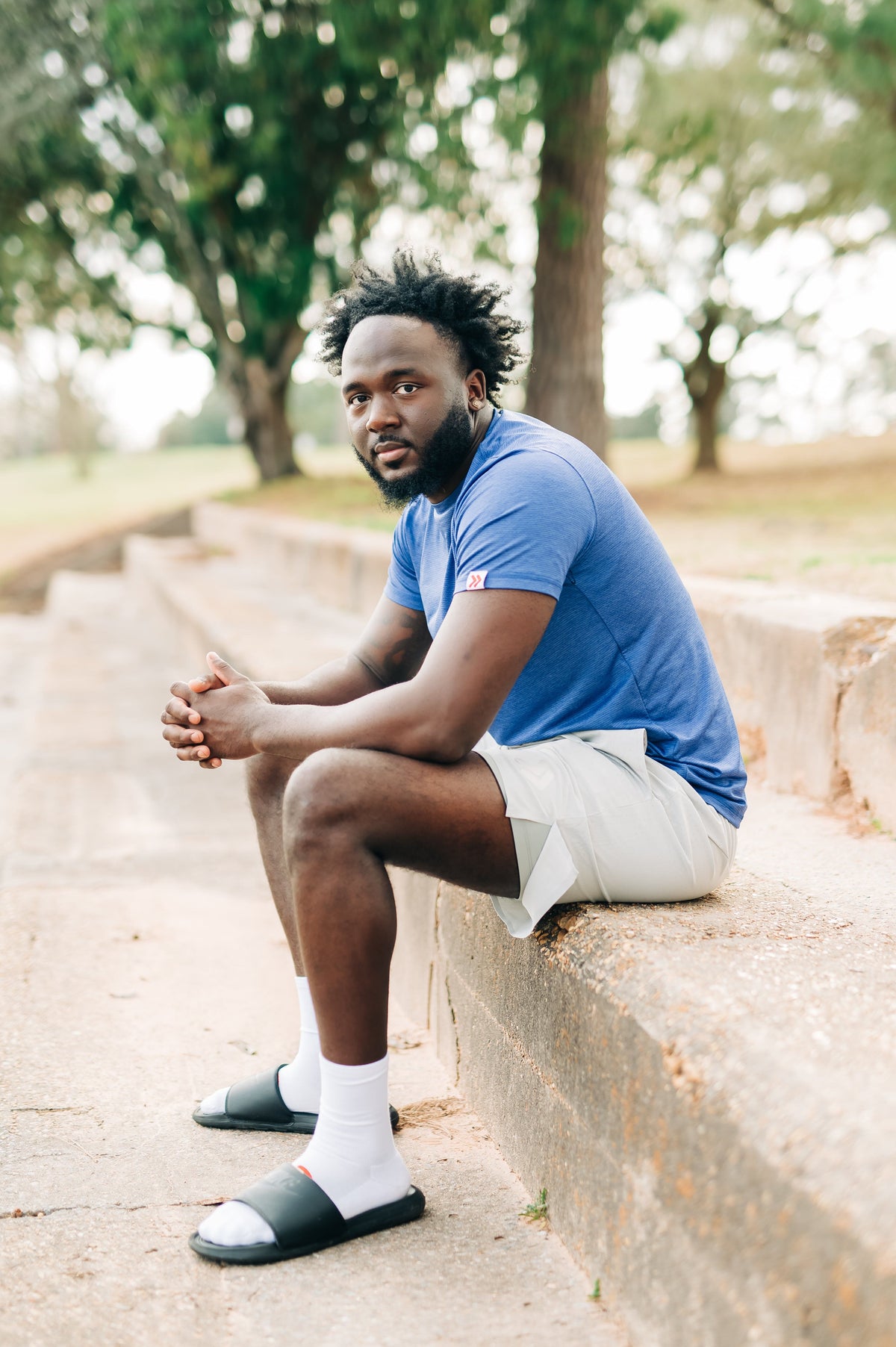Side portrait of a man wearing a blue LuxDry Training T-Shirt on a park wall.
