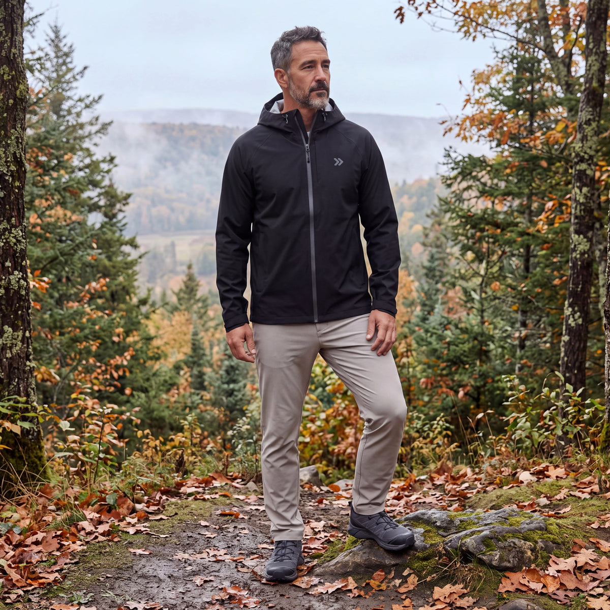 Man wearing the black MOVE Sport Apparel hooded waterproof jacket on a wooded autumn overlook.