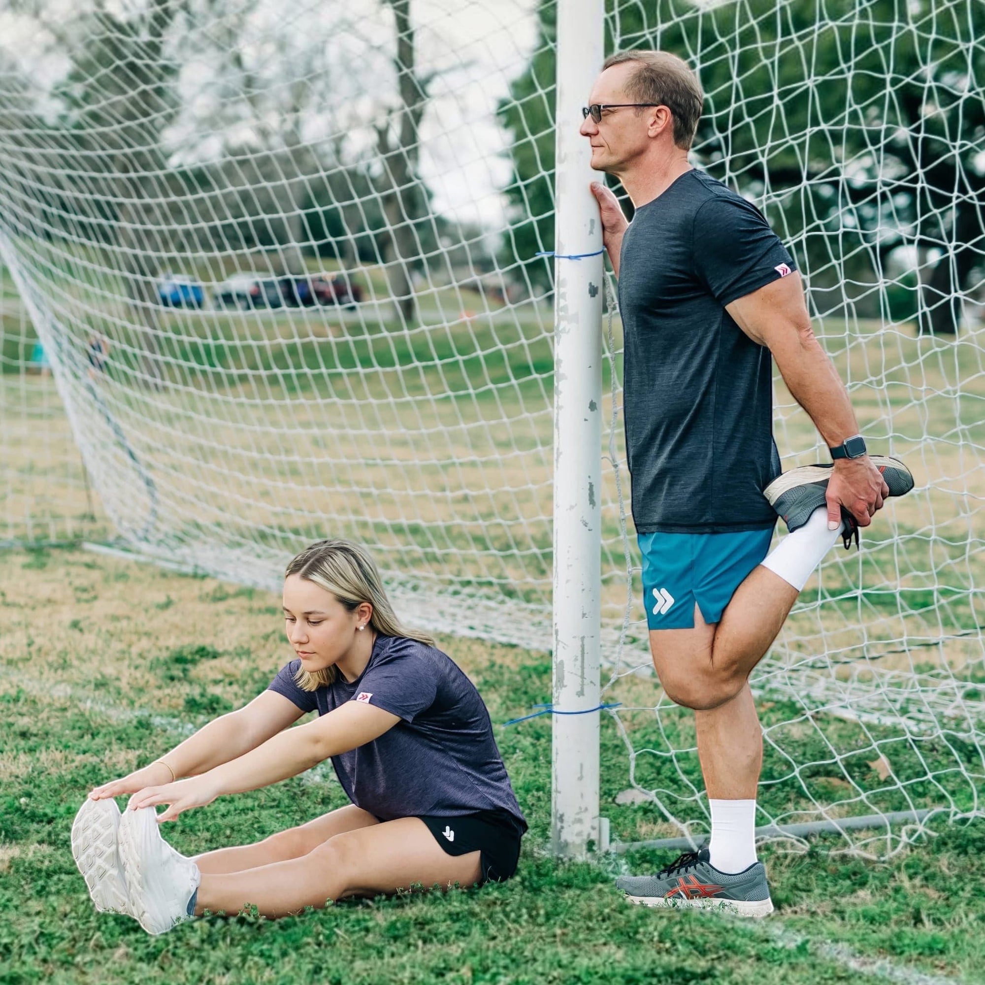 MOVE sport apparel Agility 6 inch training shorts in teal worn by a man stretching by a soccer goal on a field.