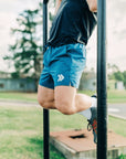 MOVE sport apparel blue 6 inch agility training shorts with boxer brief liner worn by a man doing pull-ups outdoors