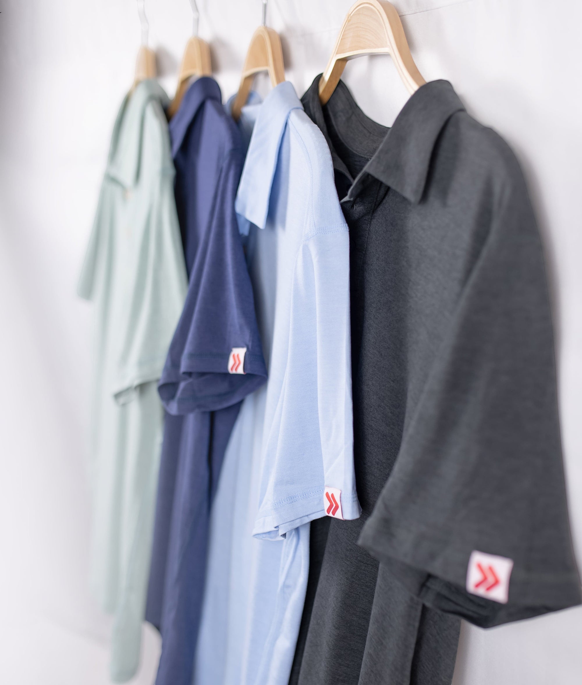 MOVE sport apparel Essential Polo Shirts in various colors hanging on wooden hangers against a white wall.