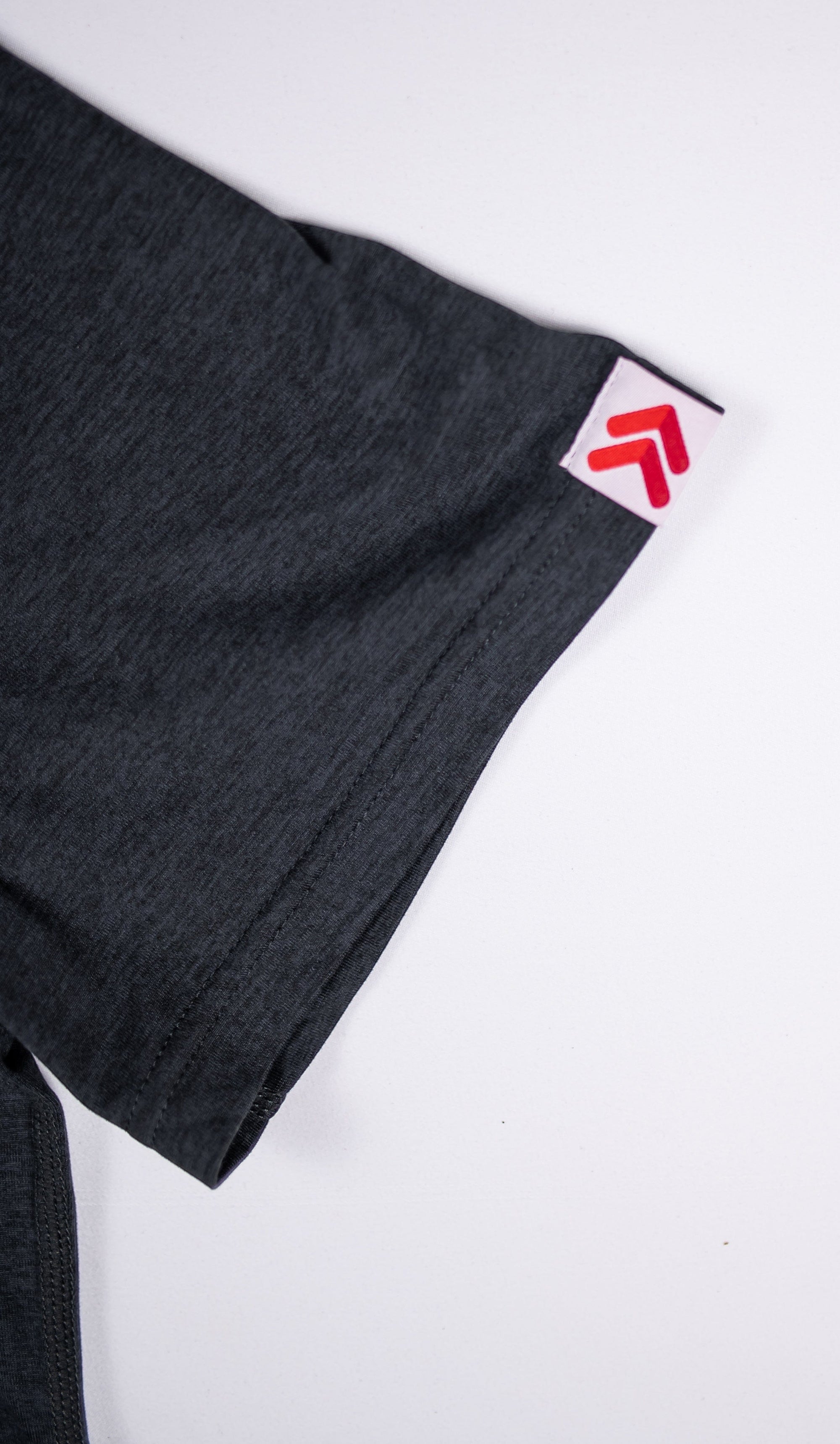 Close-up of a charcoal grey MOVE sport apparel Essential Polo Shirt sleeve with a red logo tag on the cuff