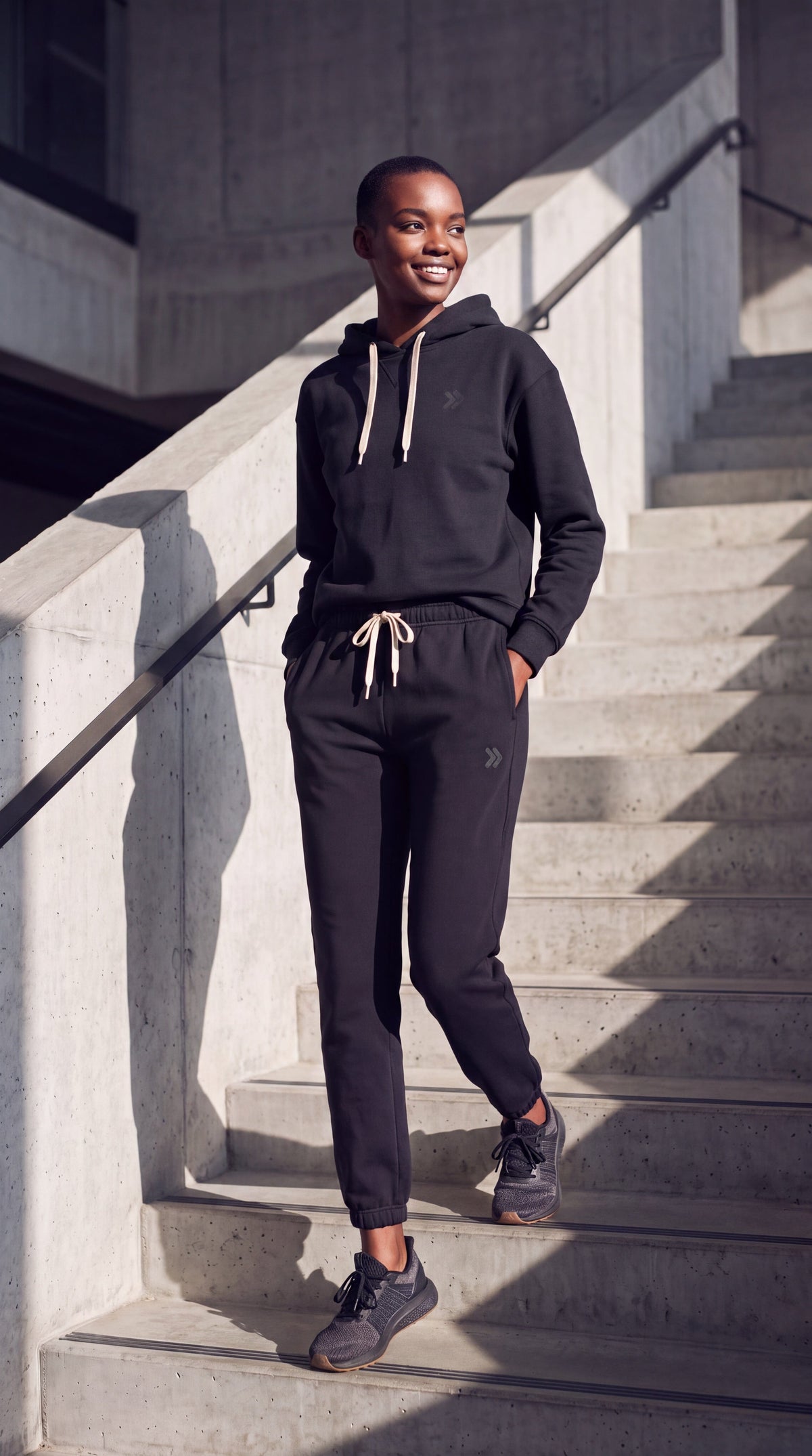 Model wearing MOVE sport apparel black French terry joggers and matching hoodie on concrete stairs