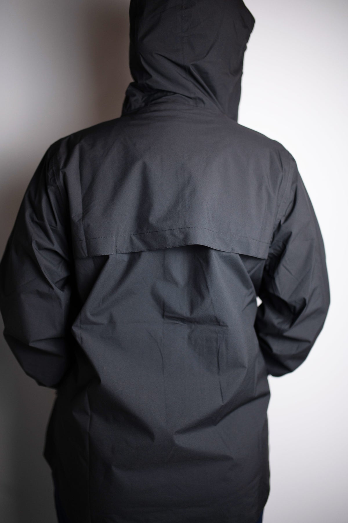 Back view of a MOVE sport apparel black lightweight waterproof packable jacket with an ergonomic hood.