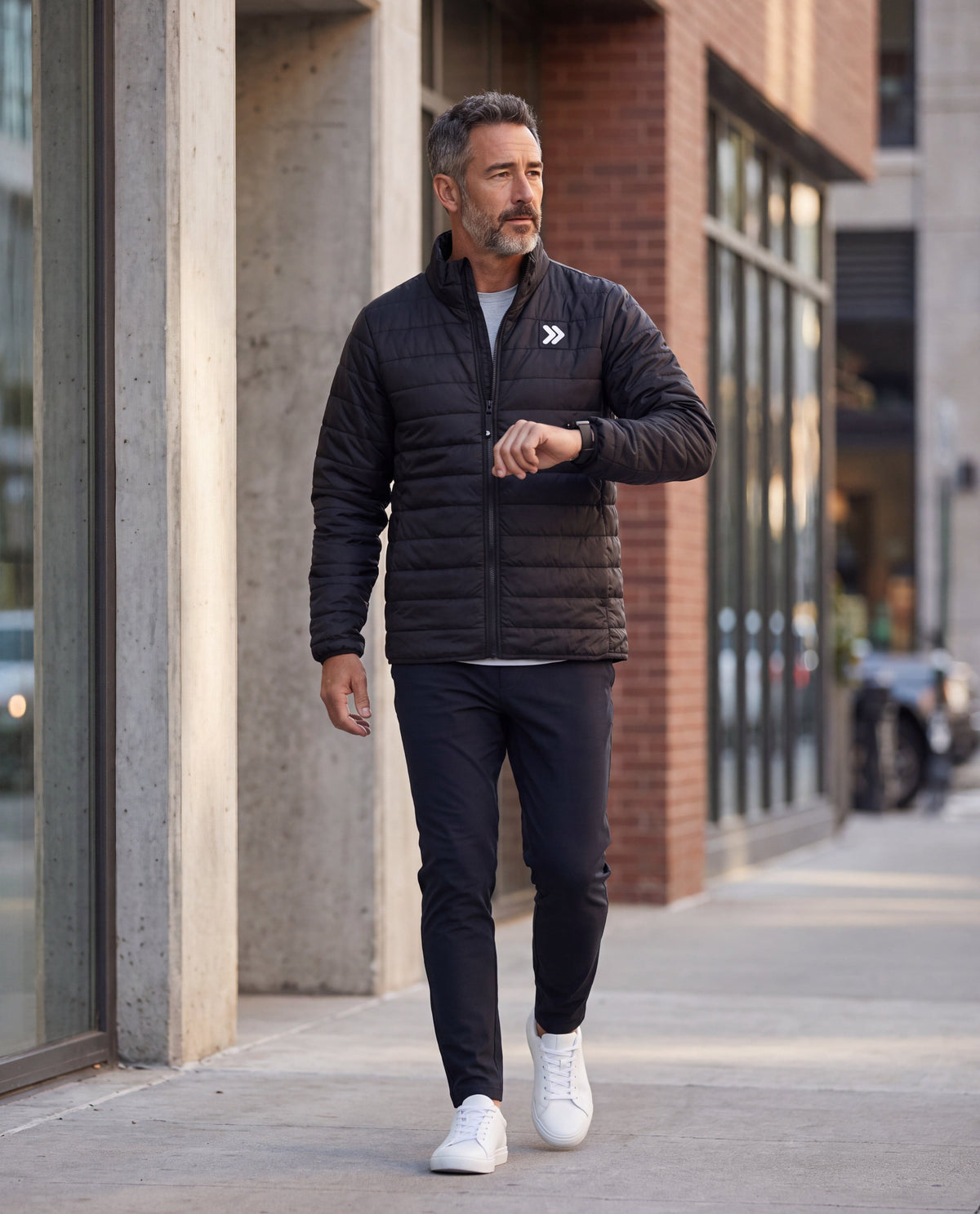 A man wearing a MOVE sport apparel black quilted lightweight down jacket with a stand-up collar, walking outdoors.