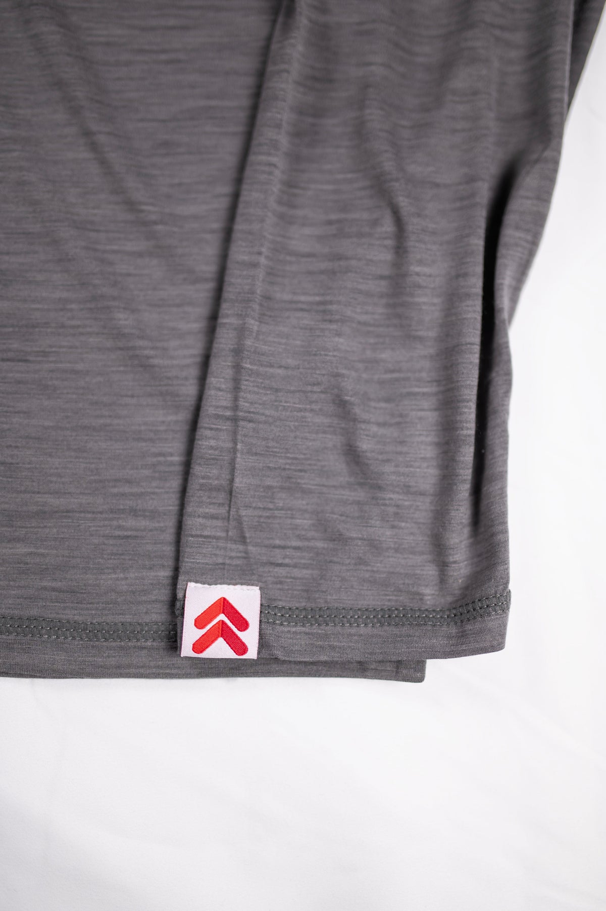 Close-up of MOVE sport apparel heathered grey merino wool long sleeve shirt featuring a red brand logo cuff tab.