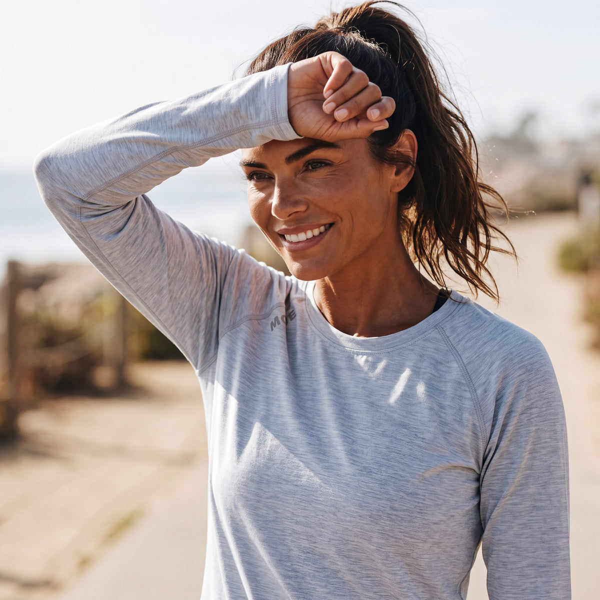 A woman wearing a MOVE sport apparel light grey long sleeve shirt with a small red logo on the cuff, outdoors.