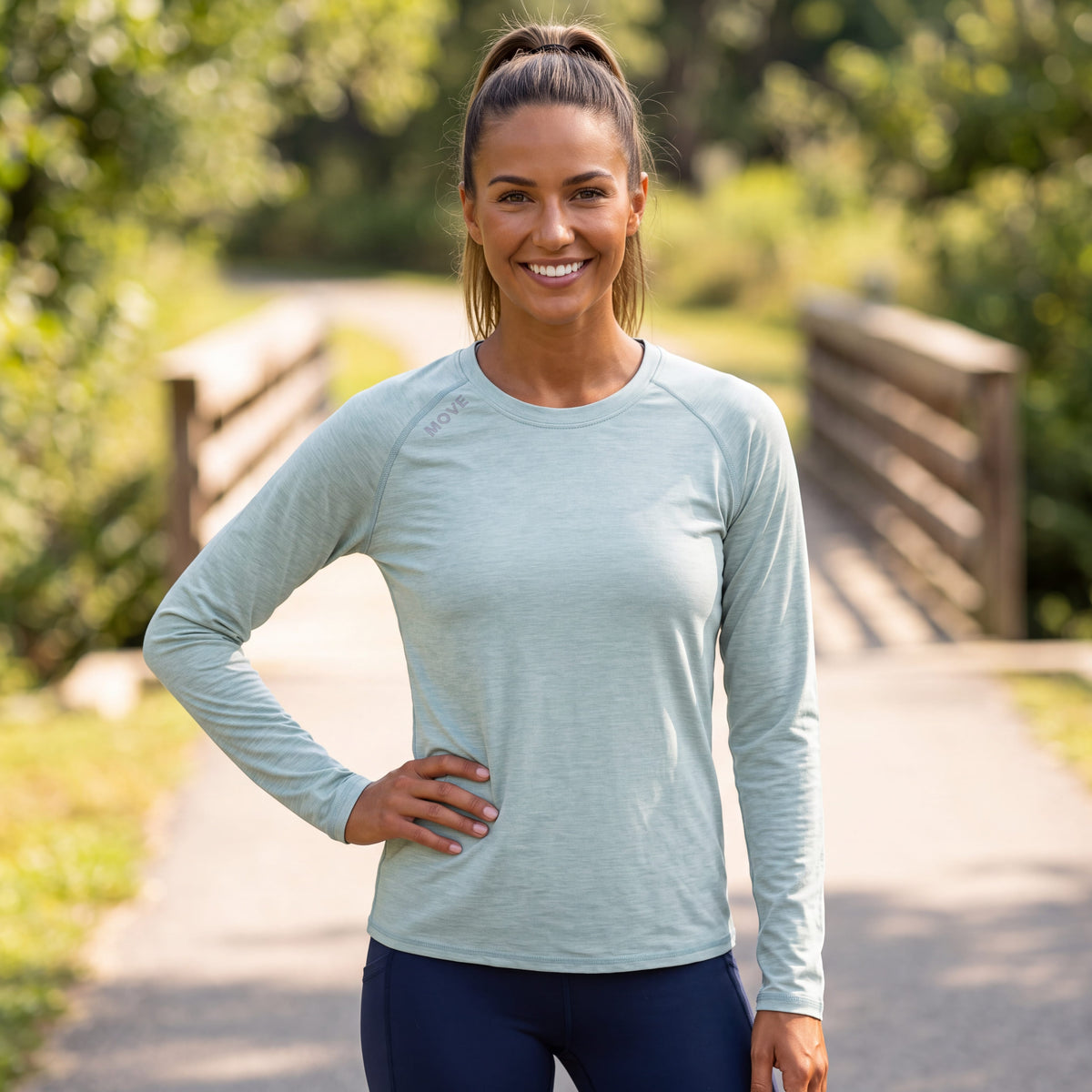 A woman wearing a MOVE sport apparel light green long sleeve shirt with raglan sleeves outdoors on a sunny path.