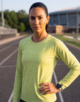 A woman wearing a lime green MOVE sport apparel long sleeve shirt on a running track at sunset.