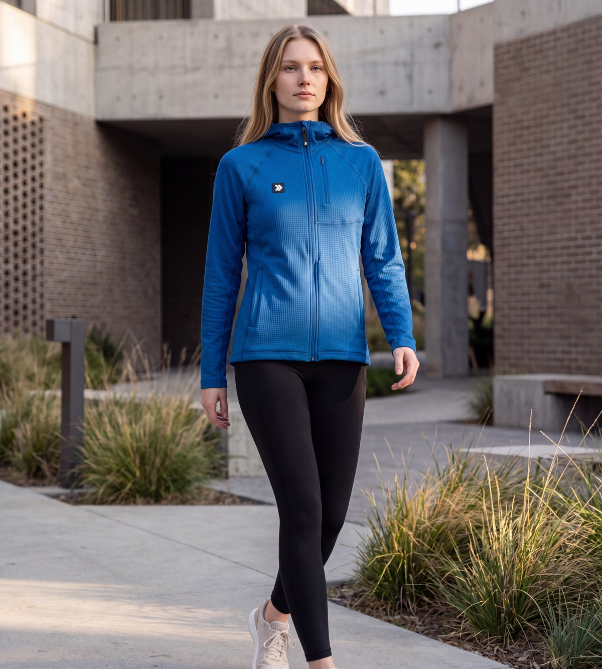 A woman wearing a MOVE sport apparel blue waffle-knit full-zip hoodie with a chest pocket, walking outdoors.