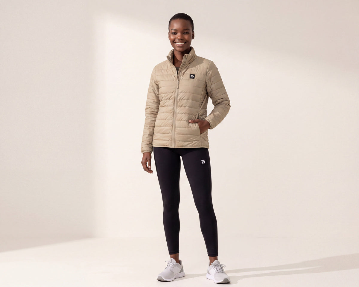 Model wearing a MOVE sport apparel beige lightweight quilted down jacket with a high neck and front zipper.