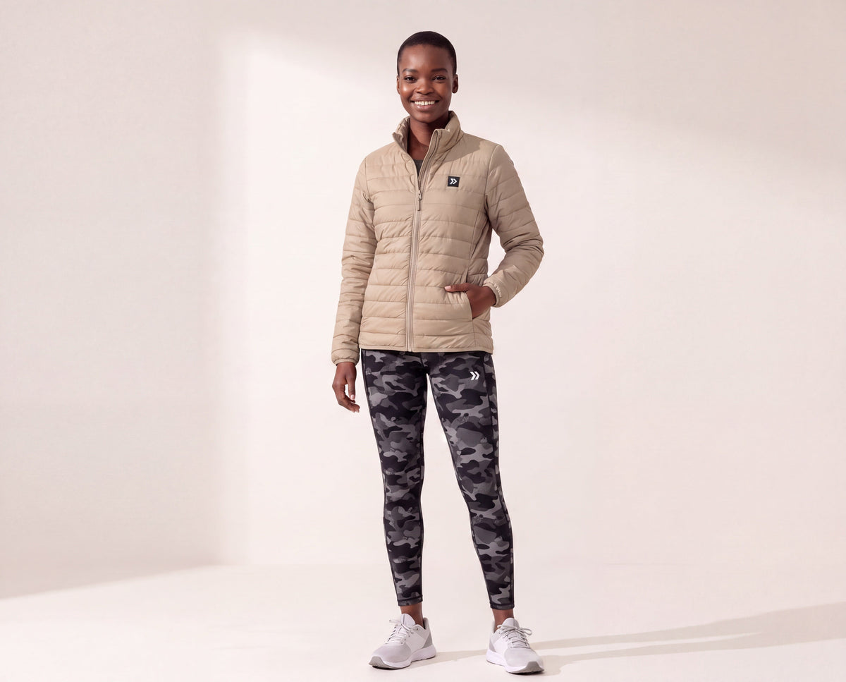 Model wearing a MOVE sport apparel beige lightweight quilted down jacket with a high neck and front zipper.
