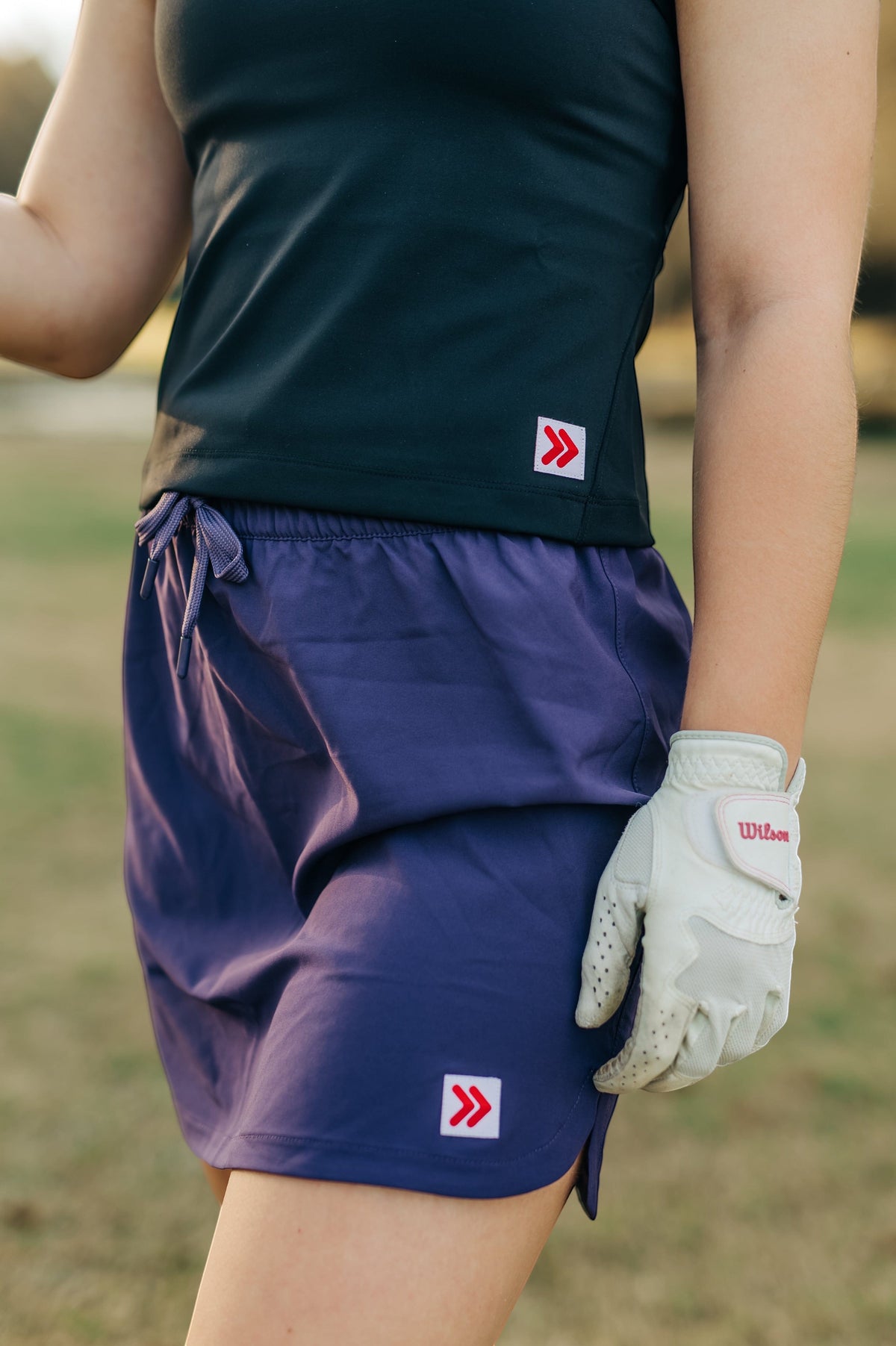 MOVE sport apparel black cropped tank top paired with a purple athletic skort and a white golf glove