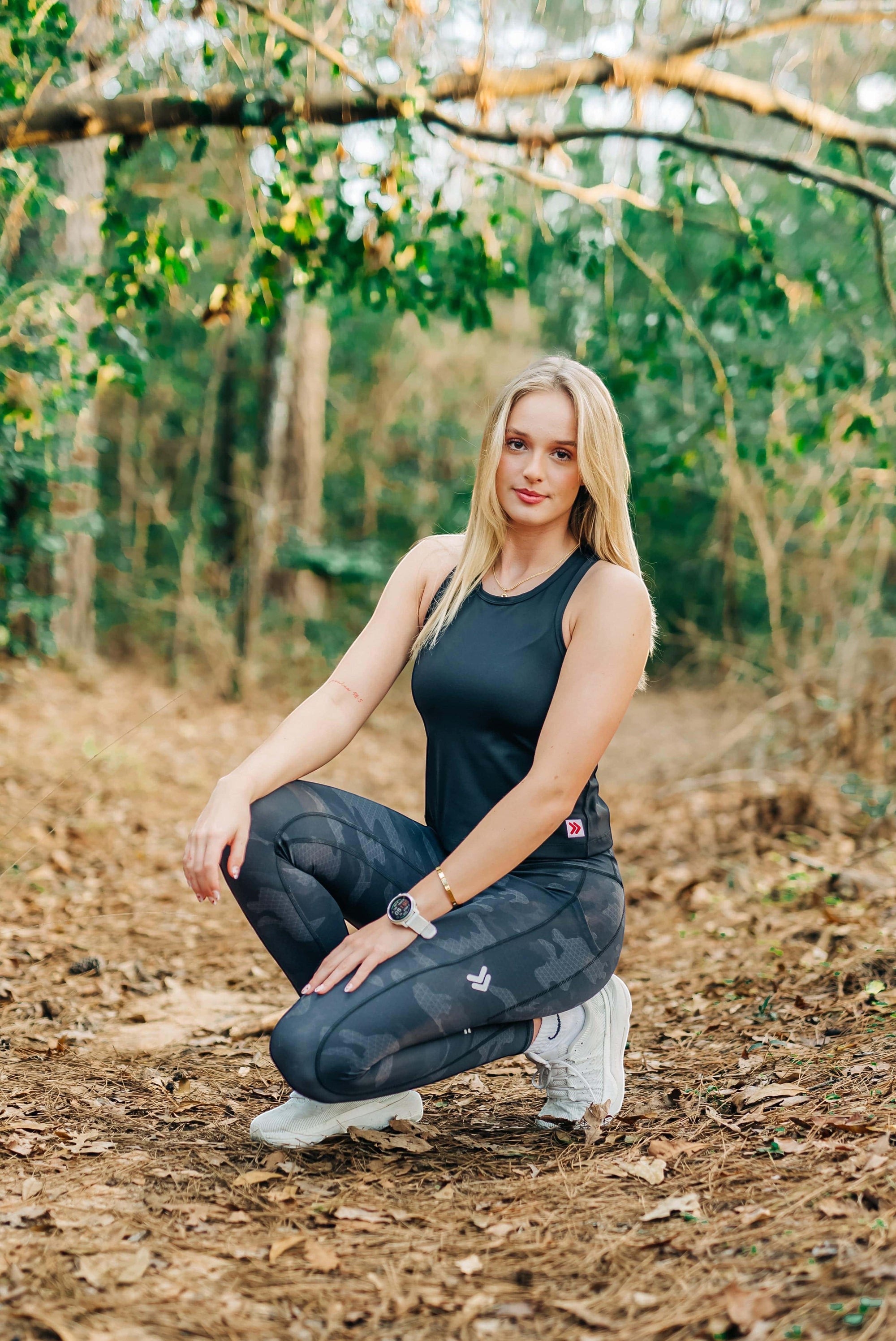 MOVE sport apparel women's black cropped tank top worn by a blonde athlete crouching in a forest setting