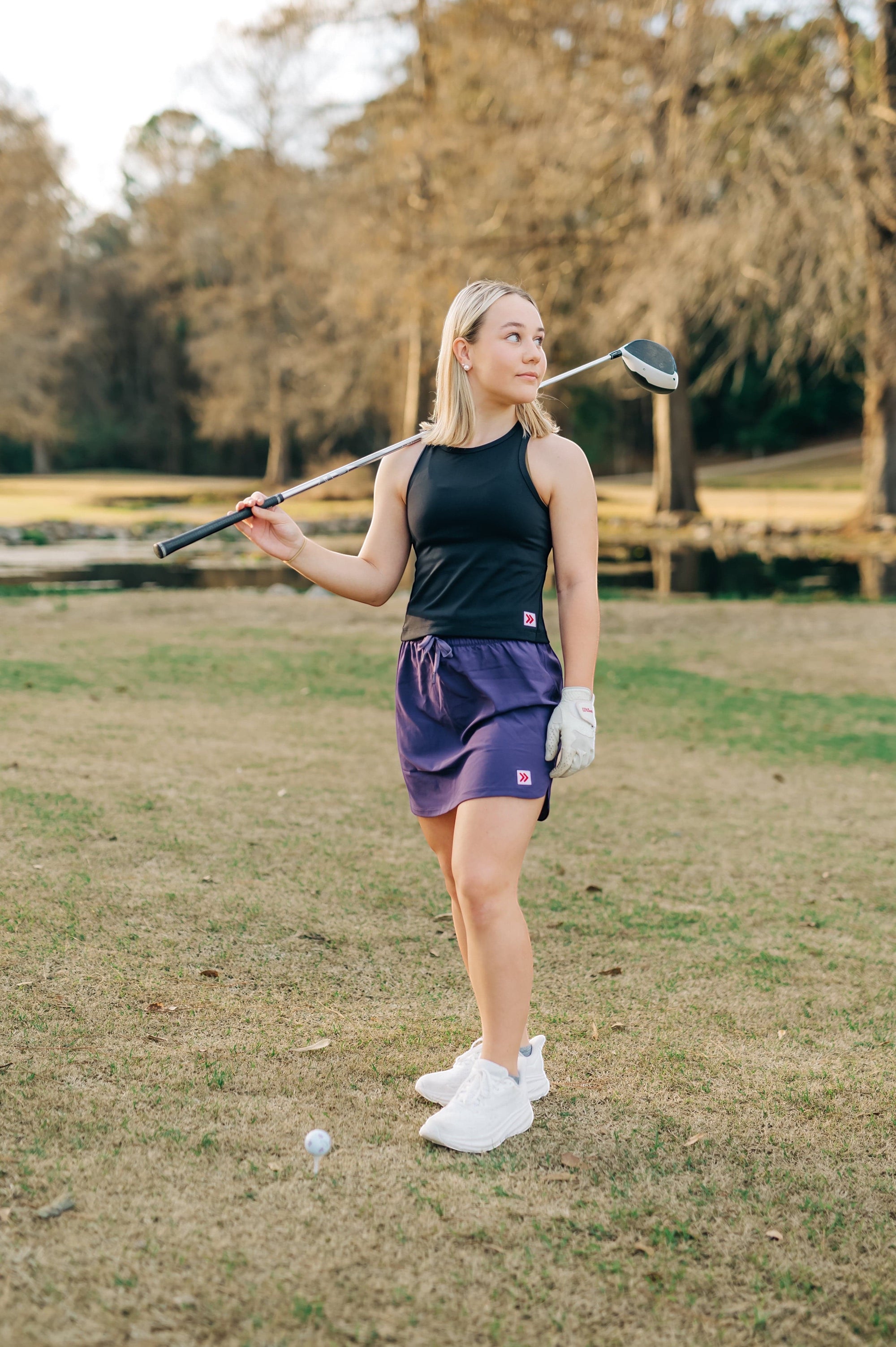 MOVE sport apparel woman wearing a black cropped tank top and purple athletic skirt on a golf course