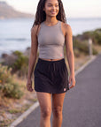 A woman wearing a MOVE sport apparel grey cropped tank top and black athletic skirt while walking outdoors.