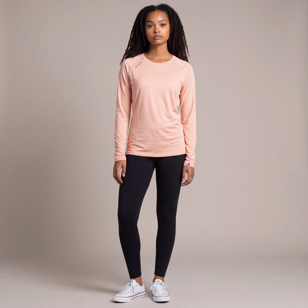 Full body neutral studio view of a woman wearing the MOVE Sport Apparel Long Sleeve LuxDry Performance Crew Neck Shirt in Creole Pink with black leggings.