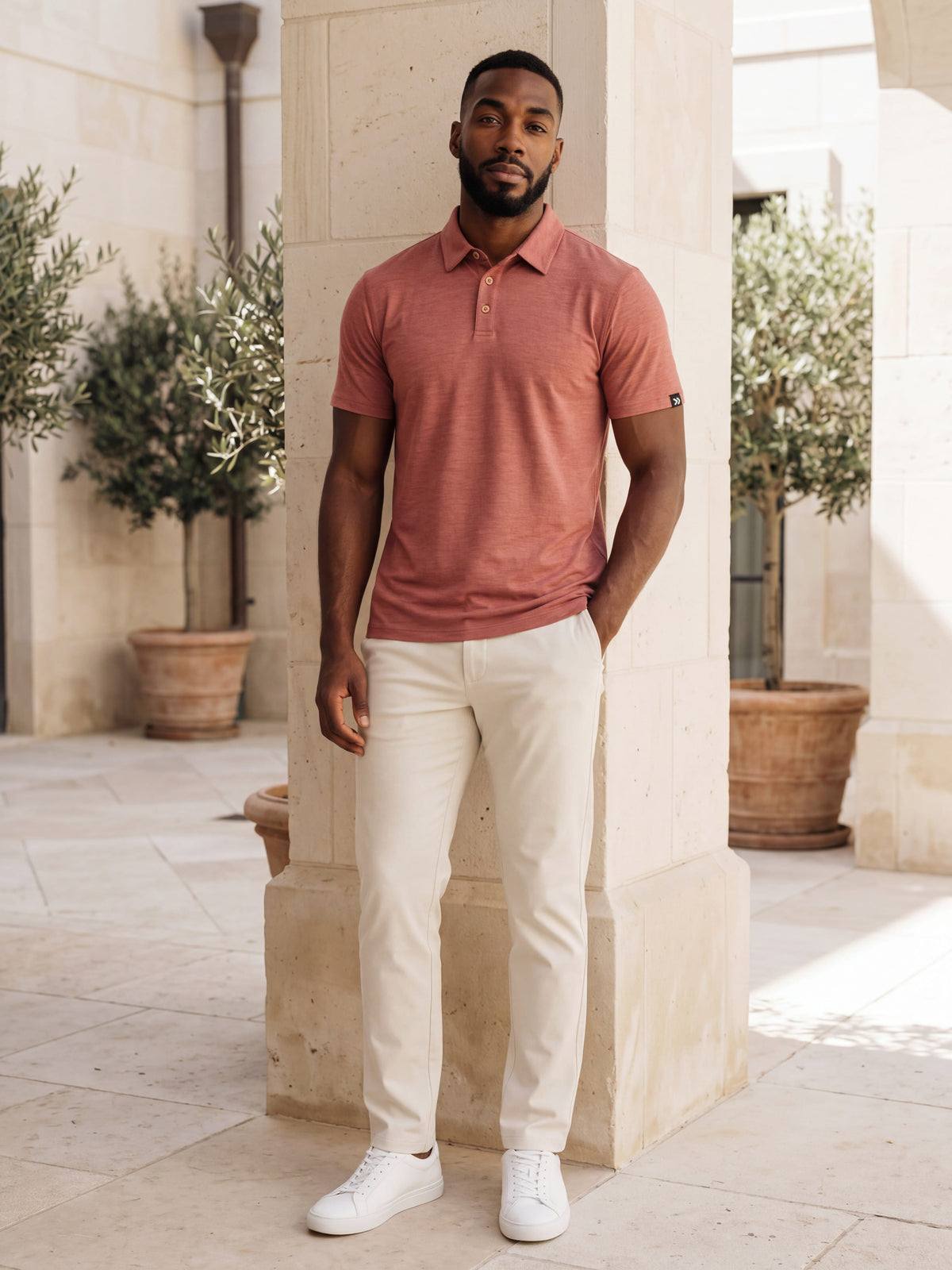 MOVE Sport Apparel Essential Polo Shirt. Man wearing the Mesa Rose polo with cream trousers in a limestone courtyard.
