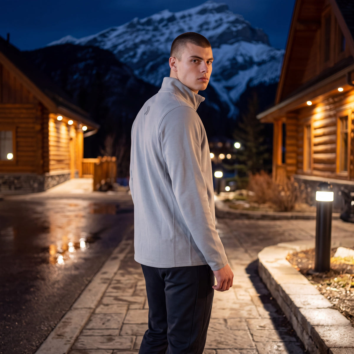 A man wearing a light grey MOVE sport apparel Cloud Quarter Zip with an embroidered logo, standing in a mountain resort
