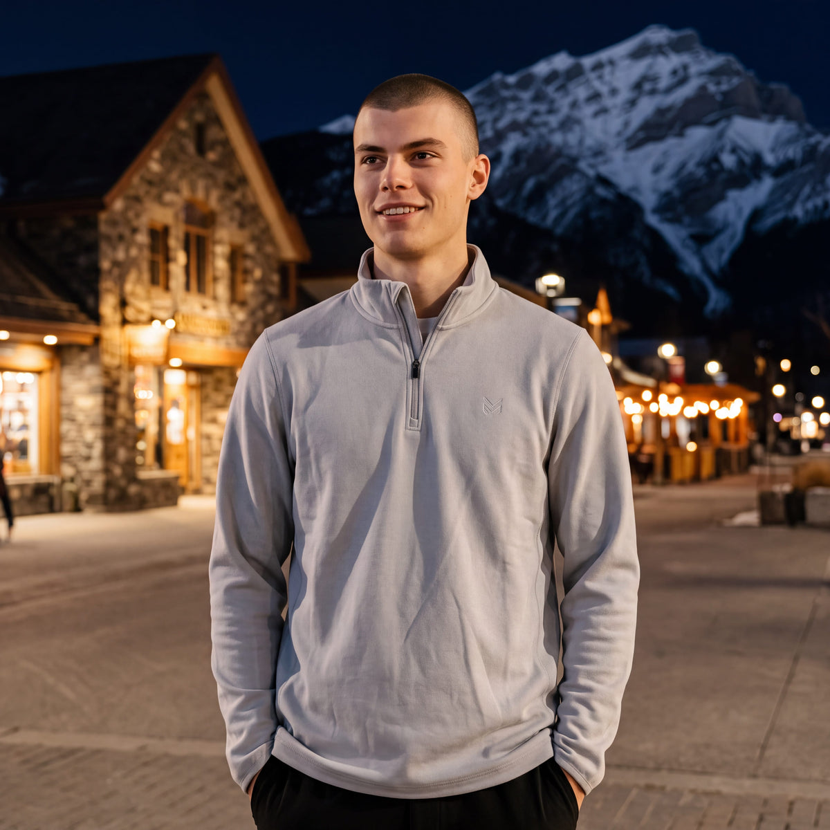 Man wearing a light grey MOVE sport apparel Cloud Quarter Zip with embroidered logo in a mountain village at night.