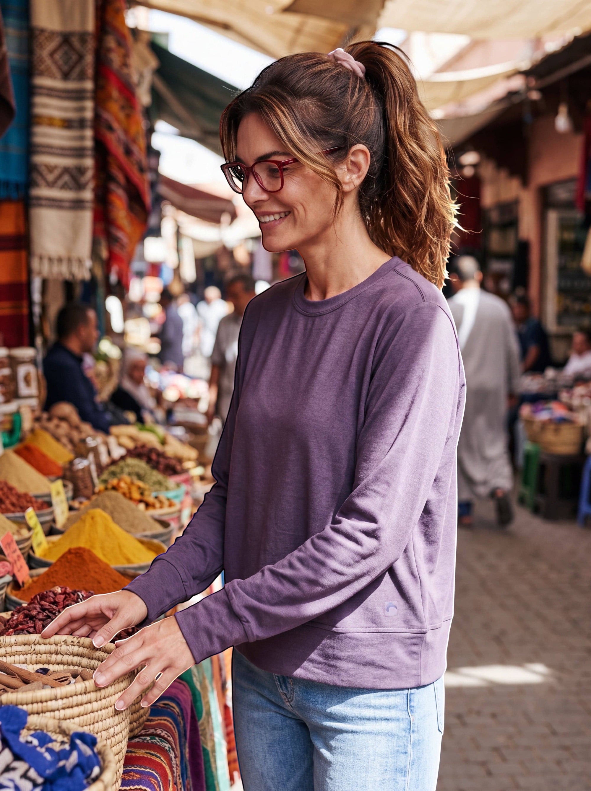 Woman wearing a MOVE sport apparel purple long sleeve crewneck pullover while shopping at a vibrant outdoor market