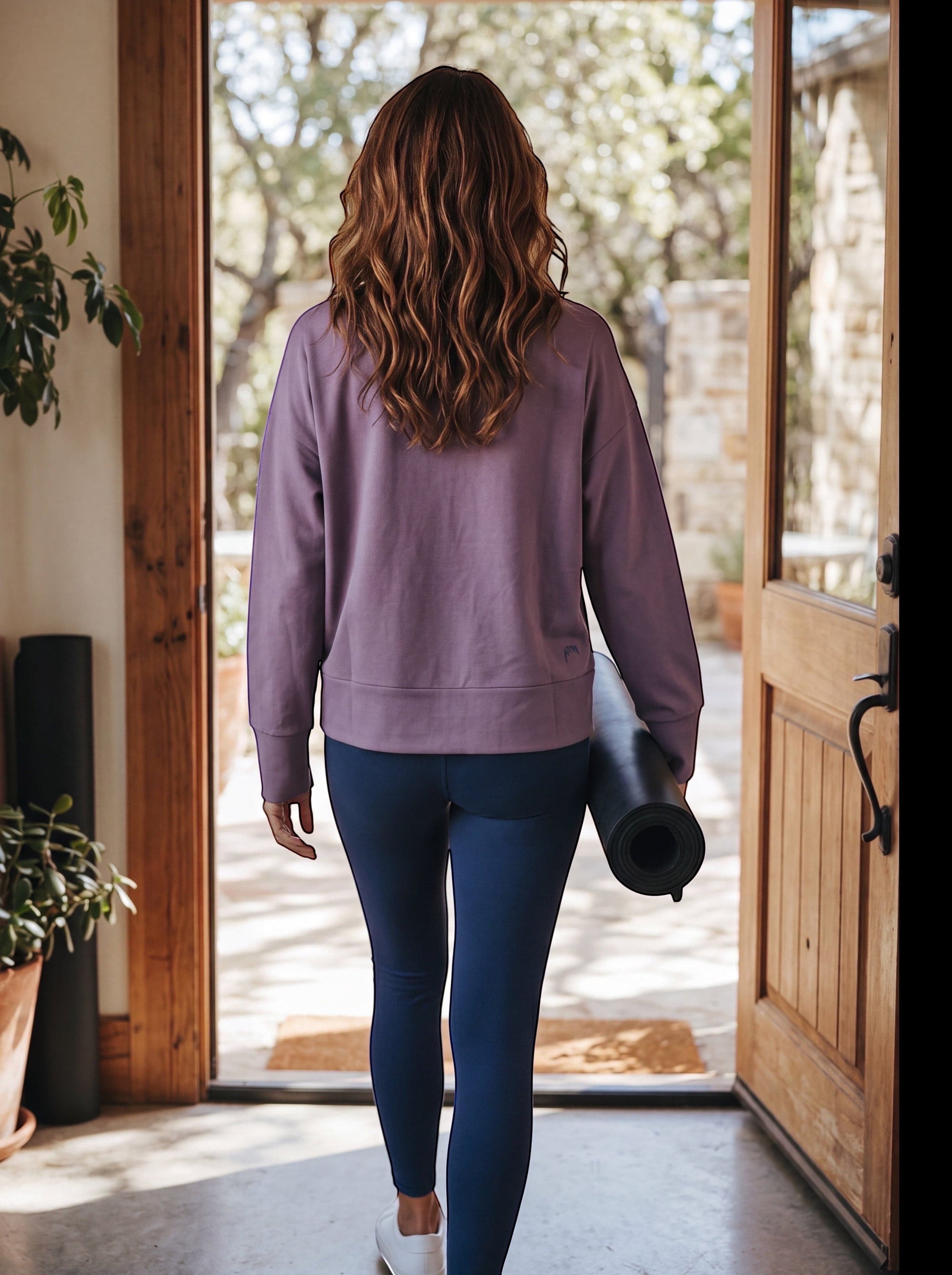Woman wearing a MOVE sport apparel purple long sleeve crewneck pullover and blue leggings, carrying a yoga mat.