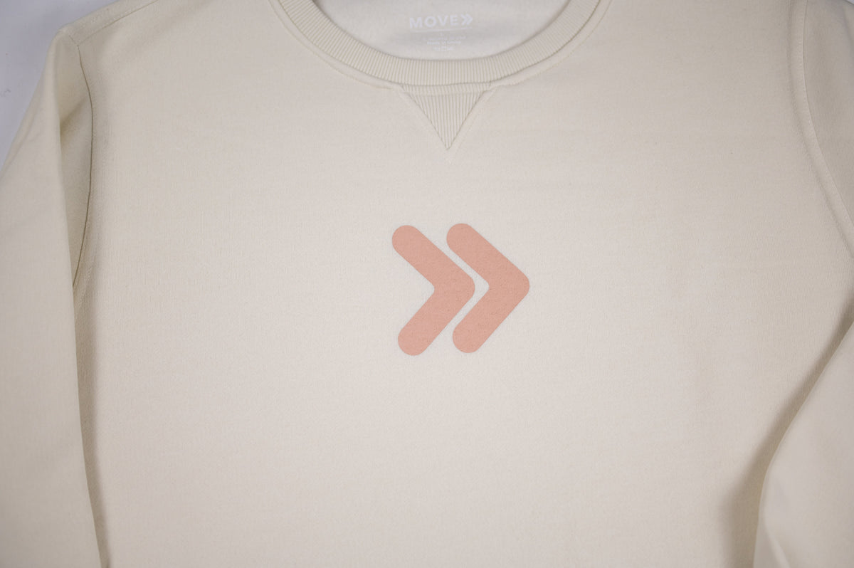 Close-up of the blush-pink double-chevron embellishment on the cream MOVE Sport Apparel Logo Sweatshirt.