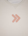 Close-up of the blush-pink double-chevron embellishment on the cream MOVE Sport Apparel Logo Sweatshirt.