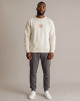 Male model wearing the cream MOVE Sport Apparel Logo Sweatshirt with charcoal joggers in a neutral studio; original blush-pink centered chest embellishment and red-and-white cuff tab retained.
