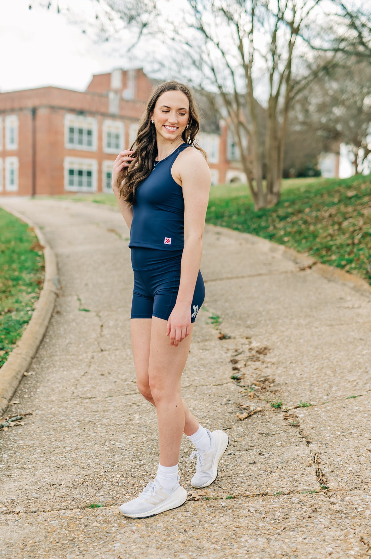 MOVE Sport Apparel women’s Biker Shorts: Woman wearing Maritime Blue biker shorts with a navy cropped tank beside a campus walkway.